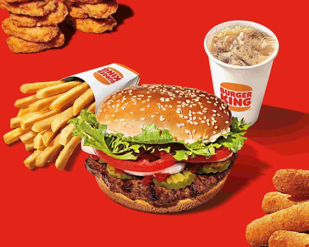 A Burger King Whopper, French fries, chicken nuggets and a soda on a red background